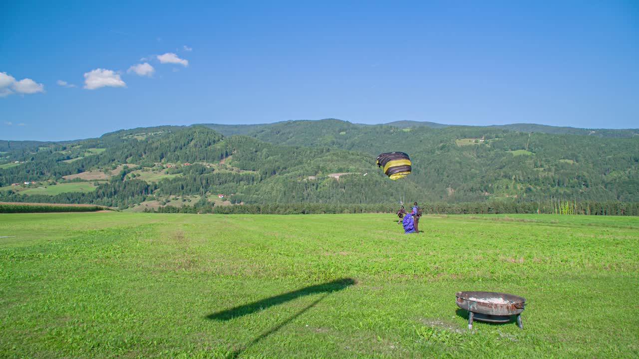 Skydiver on the way to earth lands safely, a second skydiver is waiting for him on the meadow. Tracking shot