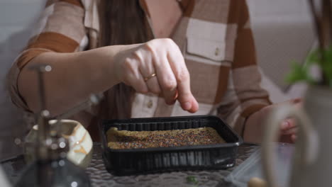nature devotee hands with golden ring spreading tiny seeds from ceramic pot onto moist growing medium in black tray before closing cover in indoor sowing ritual nurturing plant life