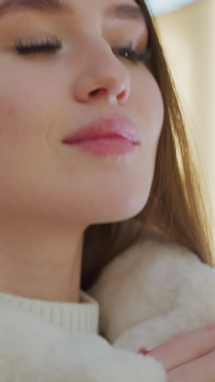 Close-up of woman hands zipping up a plush, fluffy winter jacket with a blurred background featuring warm bokeh lights and shoppers in a stylish mall