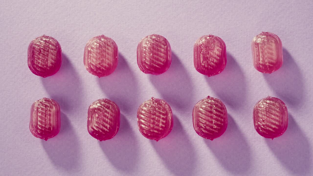 Pink lollipops, candies, bonbons on purple background. Summer bright texture studio shot for store, supermarket, close up top view, zoom. Children's favorite sweets made of sugar.