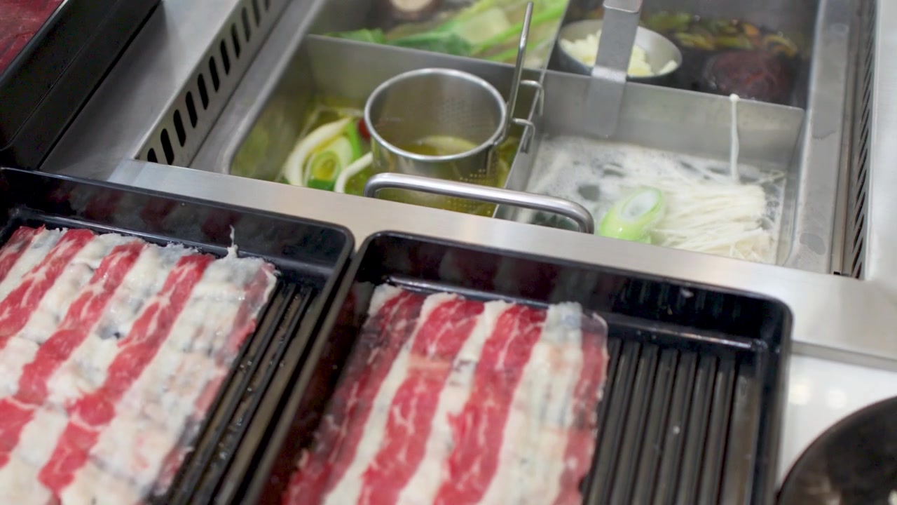 High angle shot of raw beef slices next to a boiling hot pot with vegetables