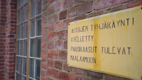 an yellow warning sign in finnish language hanging on an old red brick factory wall with windows