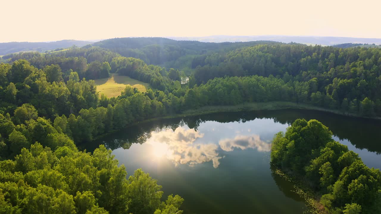 Aerial view of a beautiful Polish lake surrounded by lush forest with the sun reflecting on the water