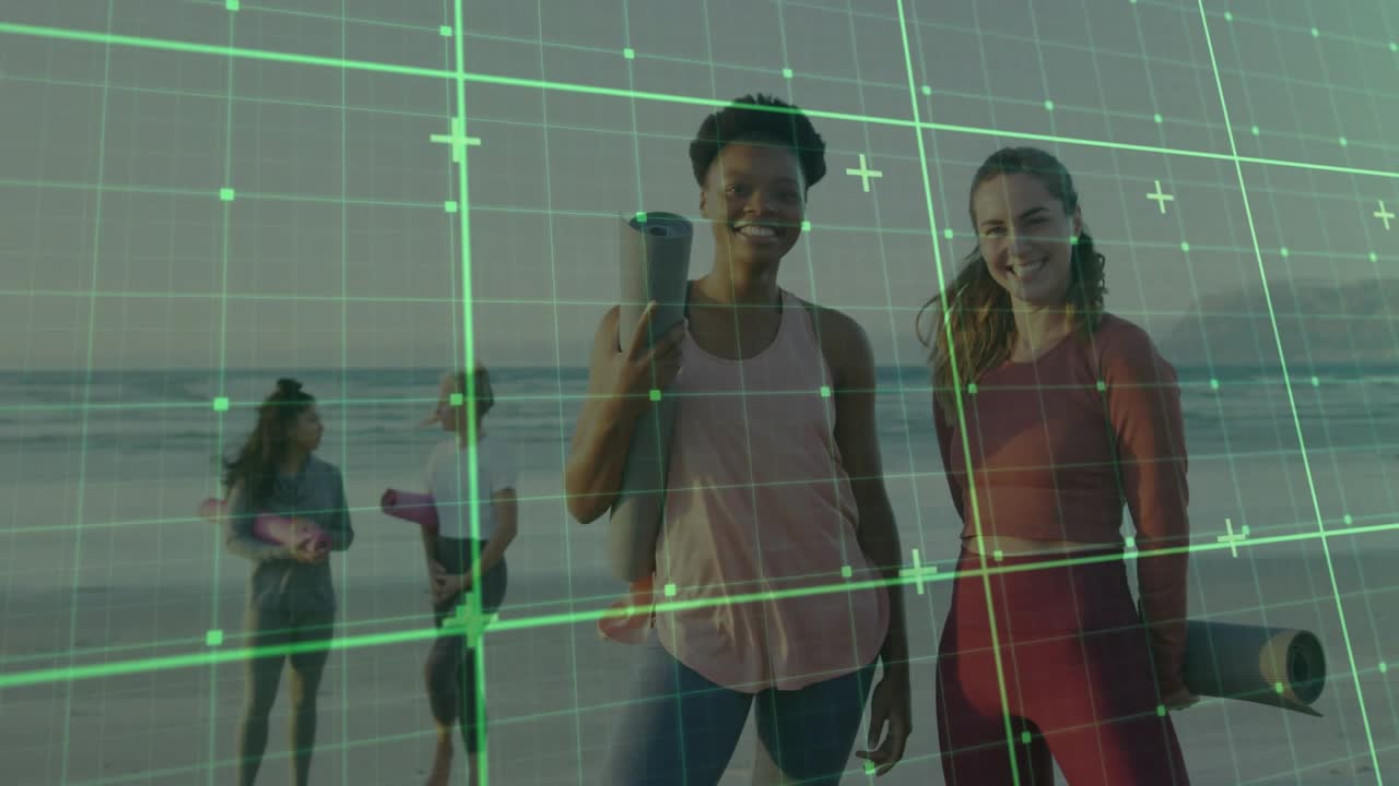 Four women holding mats walking beach toward yoga session, shifting focus to foreground duo smiling