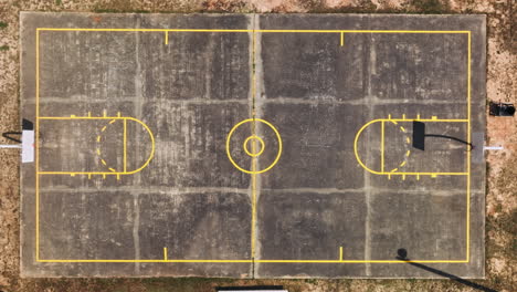 Toma-Aérea-De-Arriba-Hacia-Abajo-De-La-Vieja-Cancha-De-Baloncesto-Amateur-Vacía-Rodeada-De-Desierto-Arenoso,-América