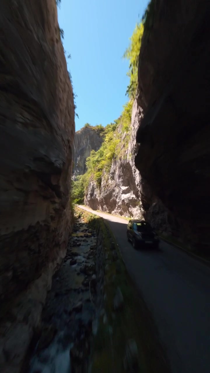 A vertical cinematic drone shot flying over a mountain river and road through a deep limestone gorge in Asturias, Spain. Highlighting sustainable tourism and natural beauty.