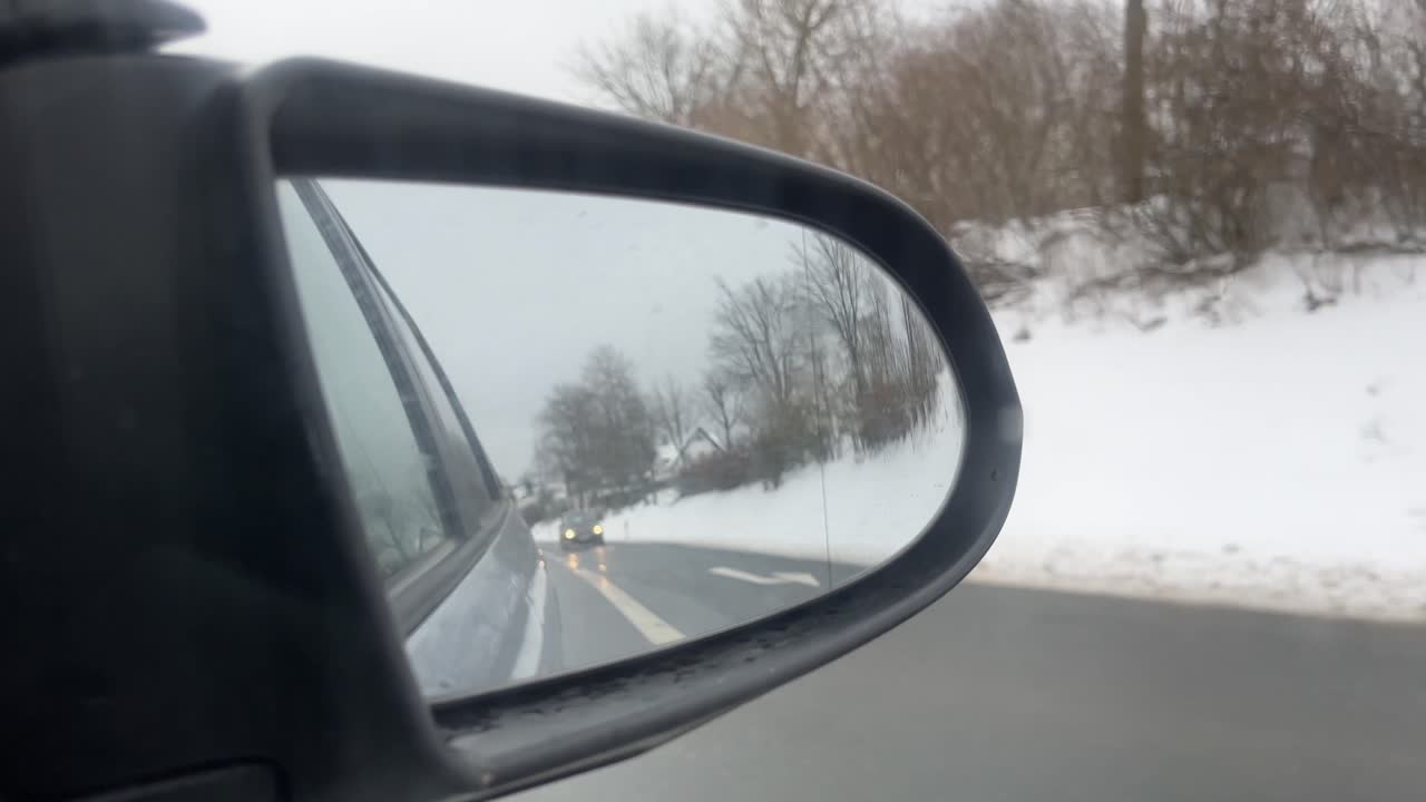 Specchietto laterale di un'auto in inverno nella neve, con un'auto che si avvicina sulla strada