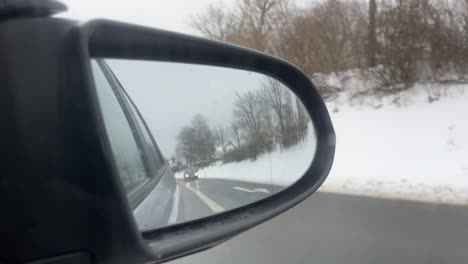 Side-mirror-of-a-car-in-winter-in-the-snow-in-which-a-car-is-approaching-on-the-road