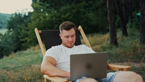 mid-aged caucasian man focused on his laptop. freelancer works in the nature sitting in the folding chair.