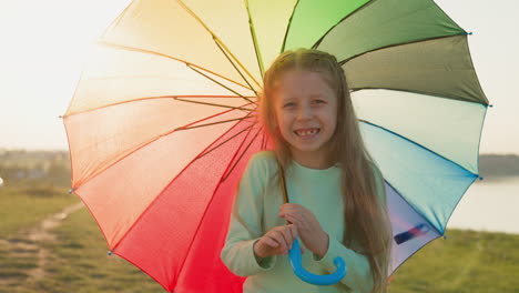 una niña feliz sonriendo bajo un paraguas arco iris