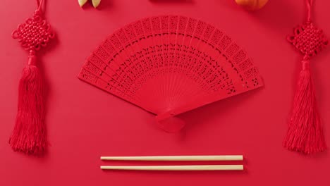 Video-of-close-up-of-chinese-fan-and-decorations-on-red-background