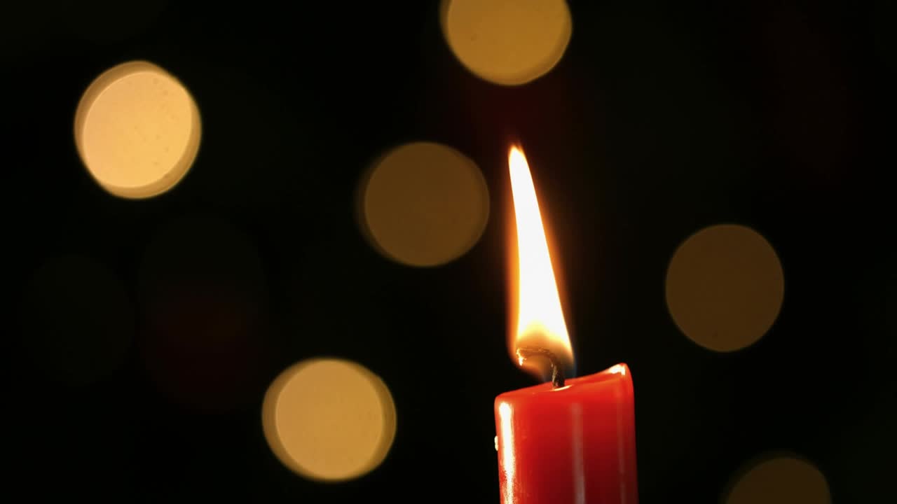 Fiamma tremolante di una candela rossa che si spegne, fumo che sale, nuvola dorata turbinante su sfondo bokeh