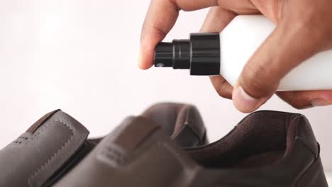 man spraying leather shoes with cleaning product