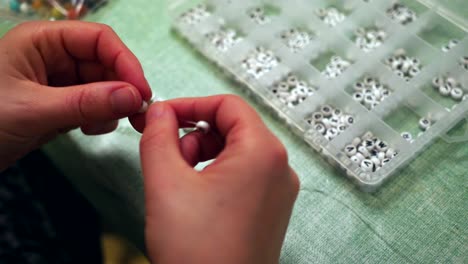 person stringing through white beads with letters to make a bracelet, close-up