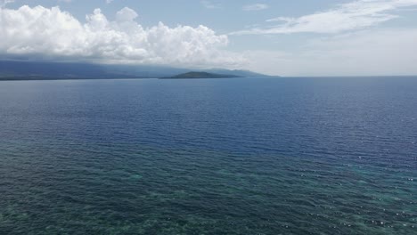 Un-Tranquilo-Mar-Azul-Con-Una-Exuberante-Isla-Verde-Bajo-Un-Cielo-Despejado,-Vista-Aérea