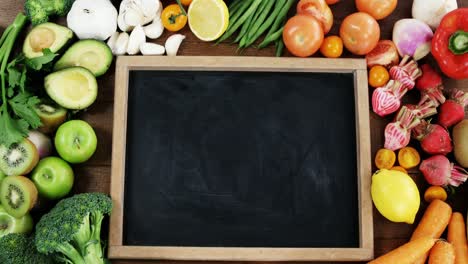 chalkboard surrounded with fresh vegetables and fruits on wooden table background