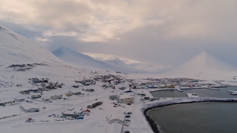 Remote Icelandic buildings covered in snow, Arctic plains stretching under winter skies near ocastal region, drone aerial establish