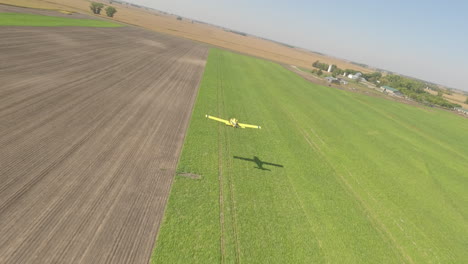 fpv drone view of small crop duster plane skimming low over rural grass runway