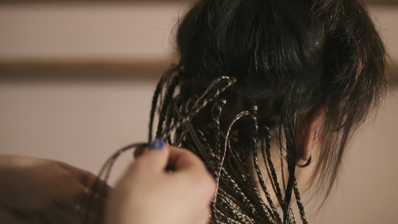 Close Up view of the hairdresser's hands doing dreads for a young woman in the hair salon. Slow Motion shot