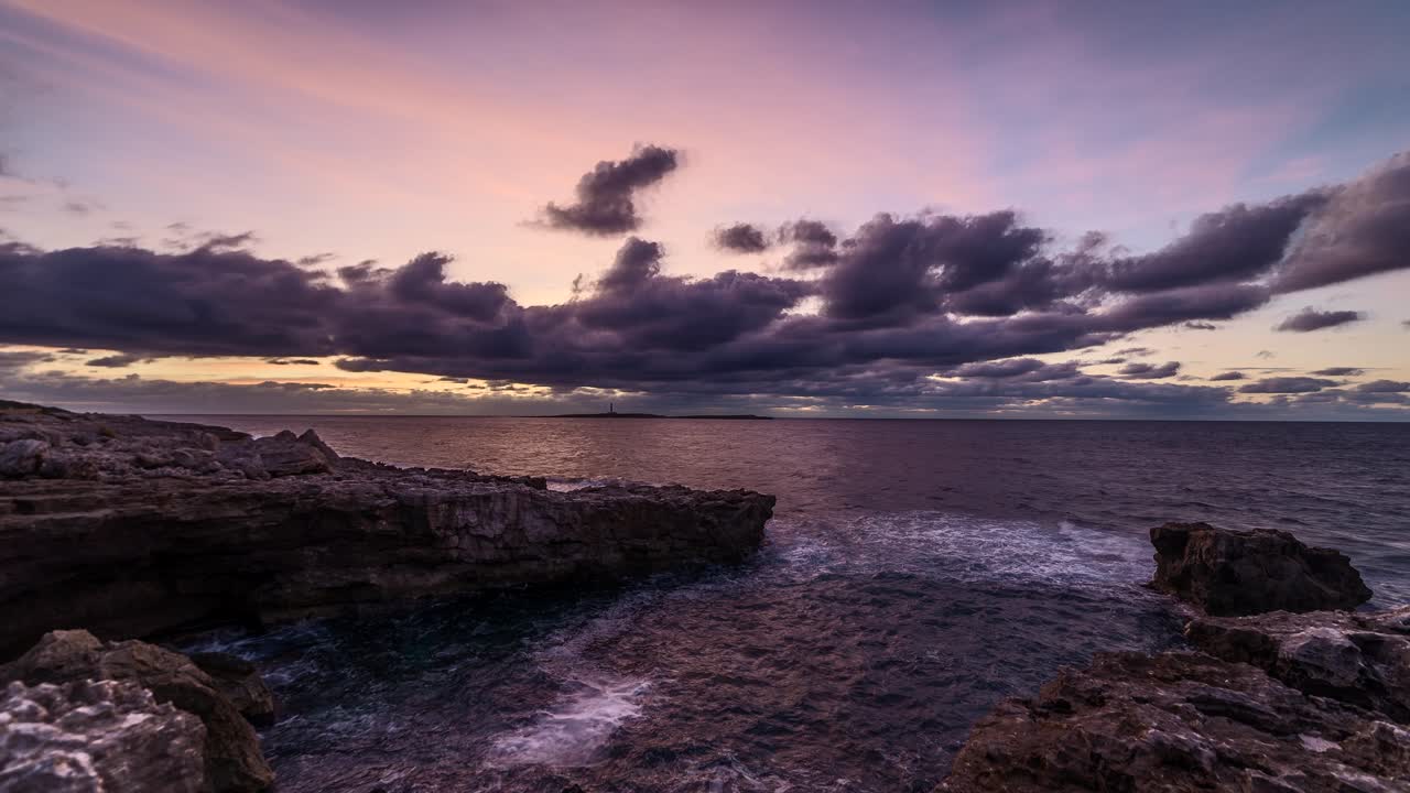 Morning clouds passing across distant Punta Prima lighthouse time lapse from rocky Sant lluis shore