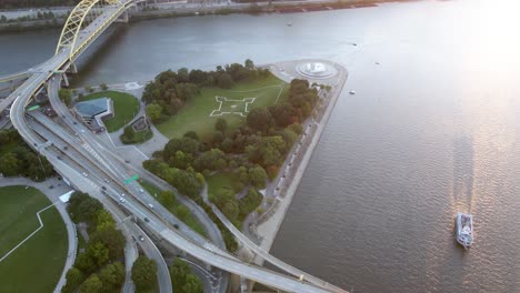 Vista-Aérea-De-Drones-Sobre-El-Tráfico-En-El-Puente-De-Fort-Duquesne,-Hacia-La-Fuente-Del-Parque-Estatal-Point,-Puesta-De-Sol-En-Pittsburgh,-Estados-Unidos