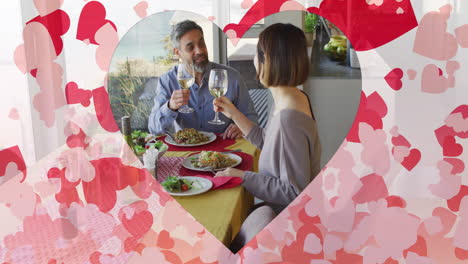 animation of hearts over diverse couple eating dinner and drinking wine at home