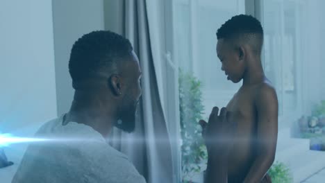 animation of lights over happy african american father and son undressing and clapping hands