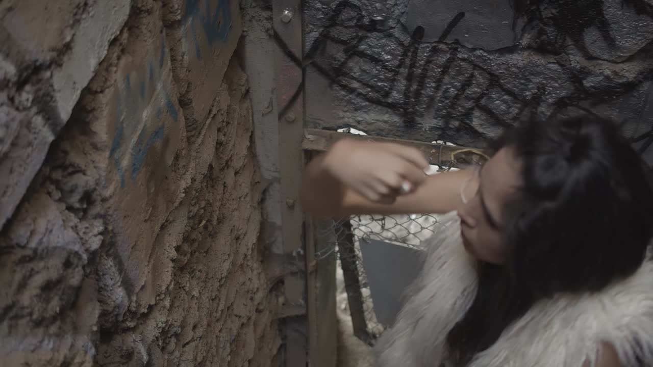 A woman with long hair and a white fur coat begins and interpretive dance inside in abandoned zoo cage