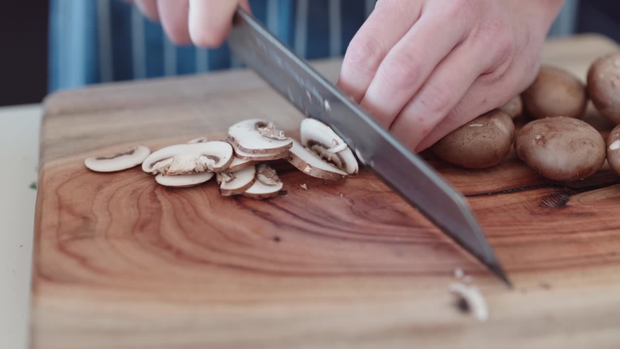 Close up of chef finely slicing swiss mushrooms on a wooden cutting board