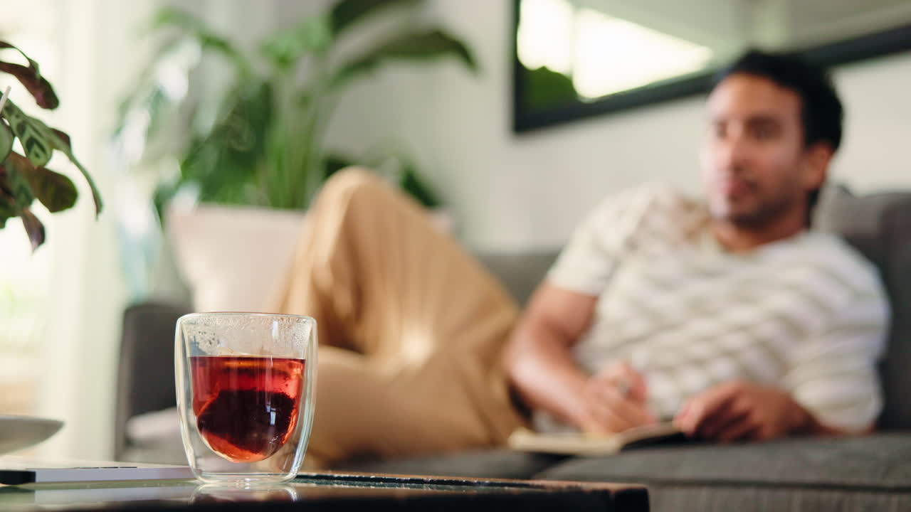 Tè caldo in infusione in un bicchiere con un uomo che scrive sul divano.