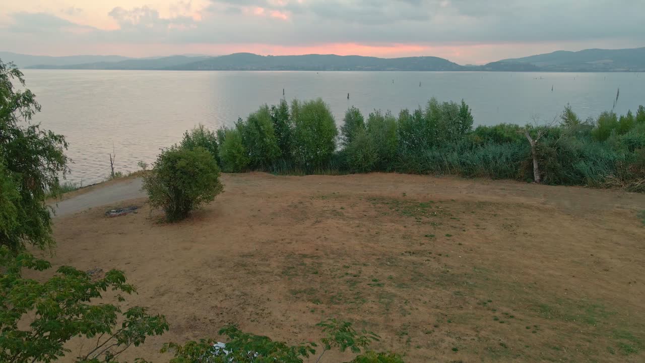 amanecer escénico en el lago trasimeno con aguas tranquilas y vegetación verde - toma aérea de drones