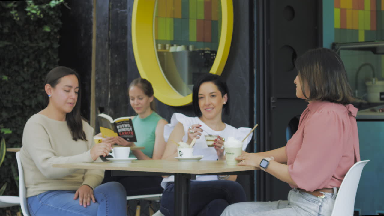 Young women enjoy ice cream and laughter while chatting and reading on a modern, colorful terrace.