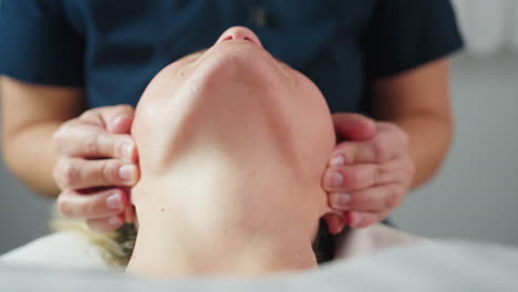 close up of skin therapist hands cradling customer jawline in bright spa room with white background during relaxing facial massage therapy highlighting expert touch and serene wellness environment