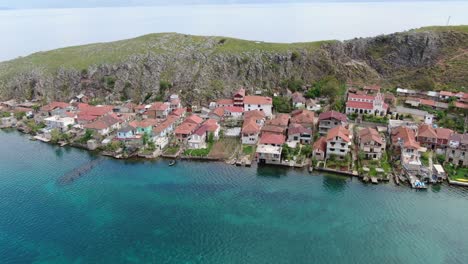 Drohnenansicht-In-Albanien,-Die-über-Eine-Kleine-Stadt-Mit-Häusern-Neben-Einem-Grünen-Hügel-Am-Ohridsee-Mit-Kristallblauem-Wasser-Fliegt