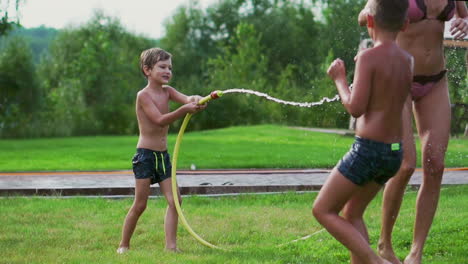 the two boys are playing with mom and dad in the backyard of their house drenching with hose water and laughing and smiling in slow motion. happy family