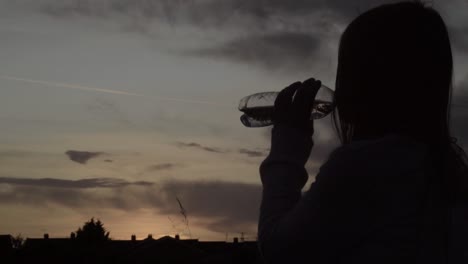 alone woman silhouette drinking bottle of water at sunset