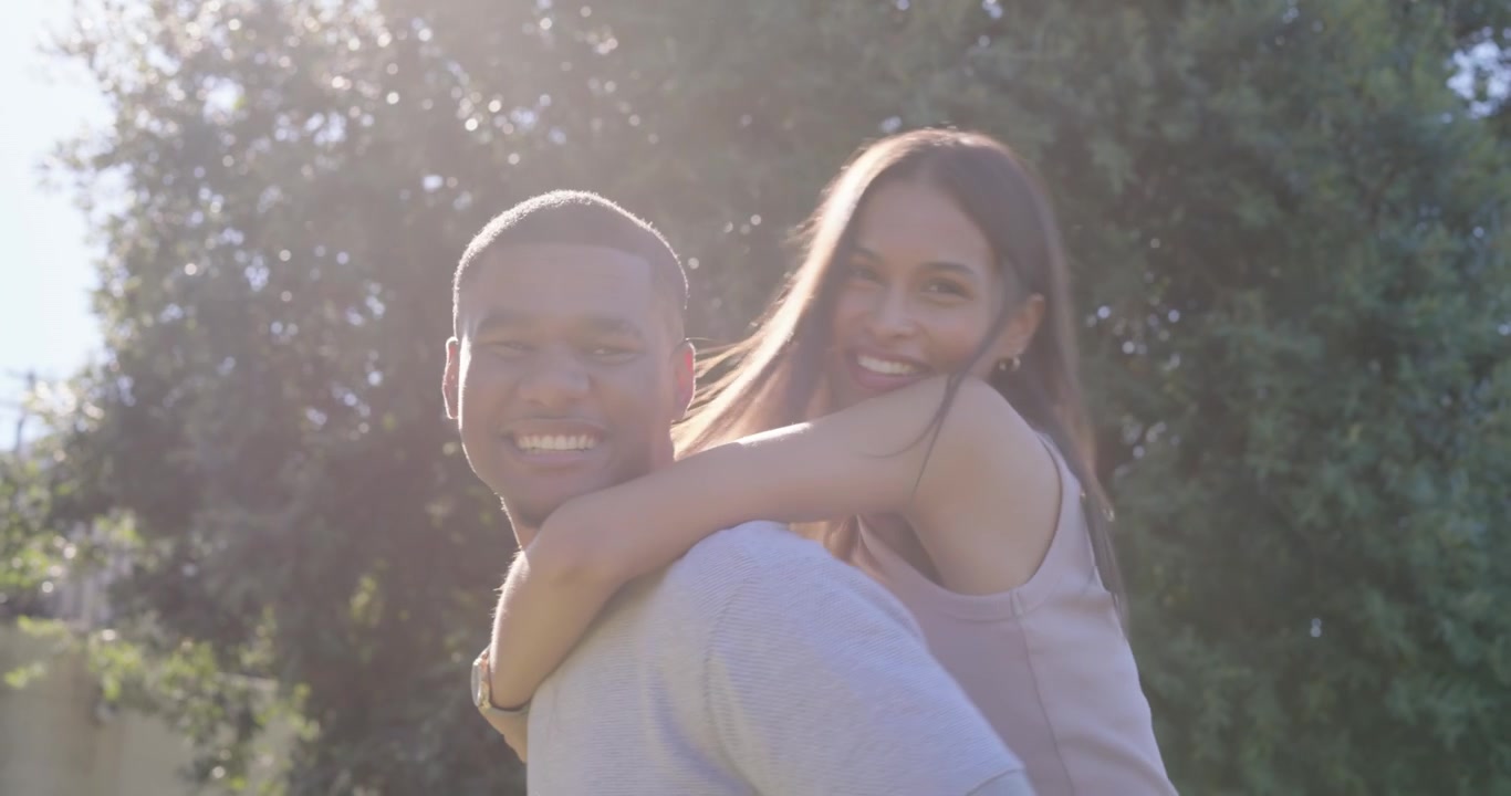 Casal afro-americano, mulher subindo nas costas do homem, homem usando relógio andando e rindo no parque