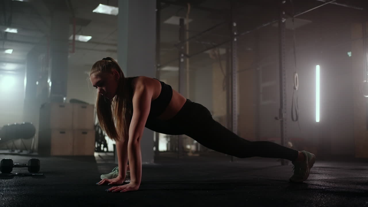 Una donna esegue esercizi di stretching in una sala fitness buia dopo un allenamento. Donna fitness che si allena sui muscoli del core in una palestra buia.