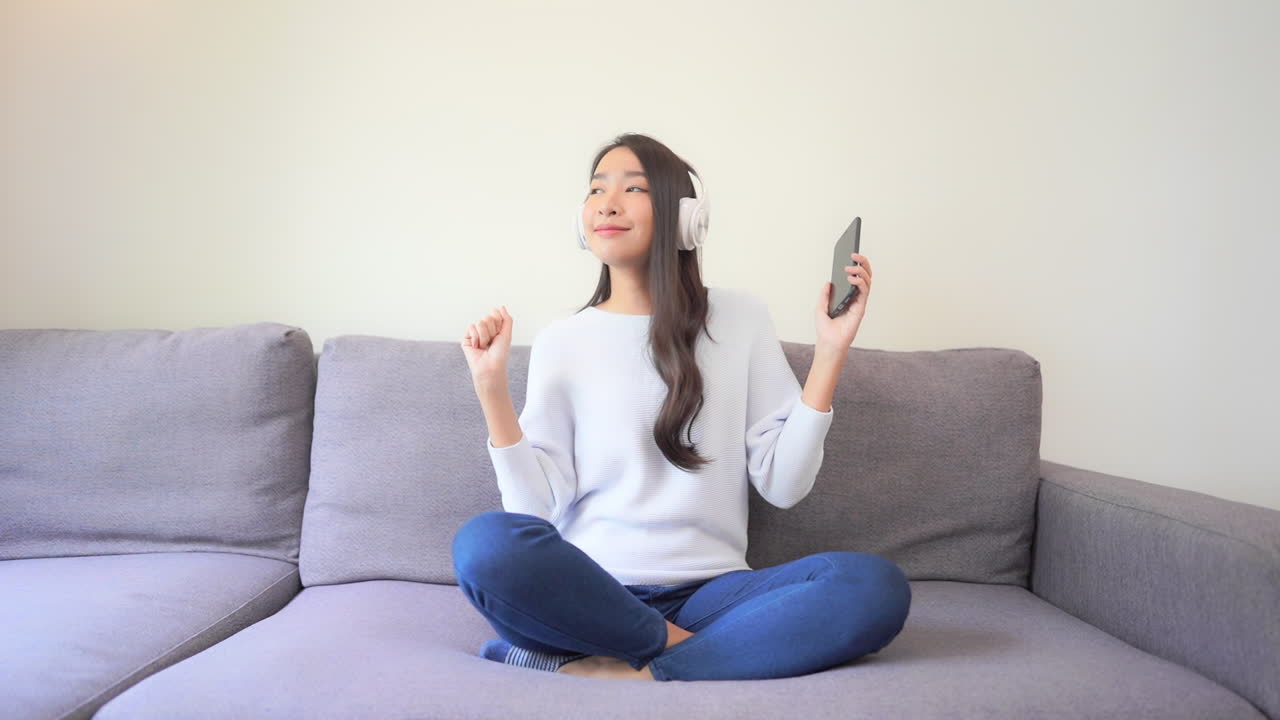 스트리밍 플랫폼에서 음악 듣기, 좋아하는 노래의 리듬에 맞춰 헤드폰과 스마트폰 춤을 추는 행복한 아시아 여성, 전체 프레임 느린 동작