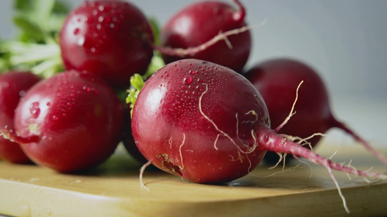 Shifting camera bringing red radish cluster into sharper focus on wooden board, revealing droplets