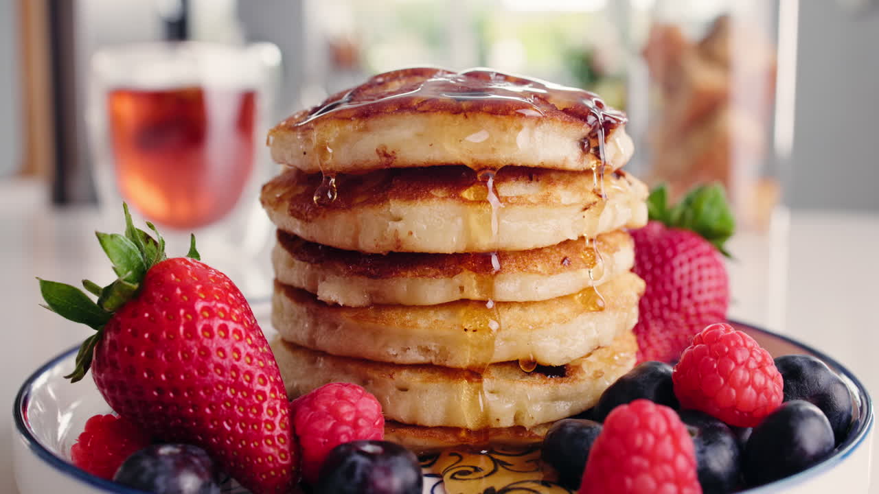 Calda sendo derramada sobre pilha de panquecas com frutas vermelhas frescas