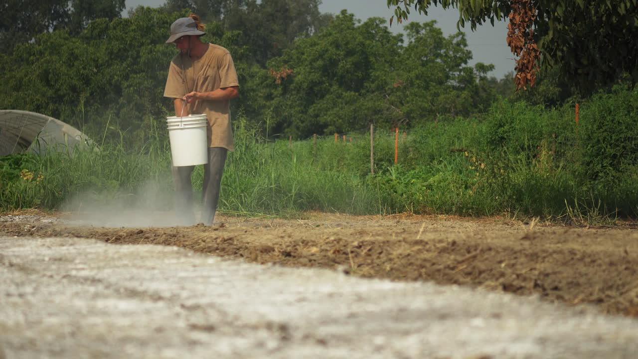 Vista frontale di un agricoltore che aggiunge fertilizzante al terreno mentre prepara il campo per la coltivazione.