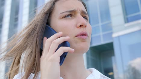 assertive woman talks on the phone outside the office: having a conversation with a smartphone