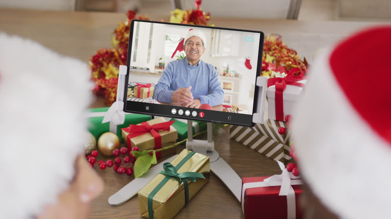 una pareja diversa con sombreros de santa haciendo una llamada de video de tableta con un hombre biracial