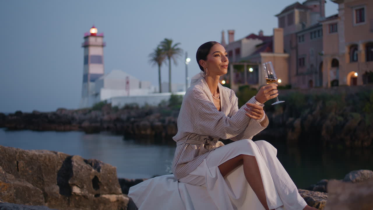mujer disfrutando de una bebida junto al faro de la costa al atardecer