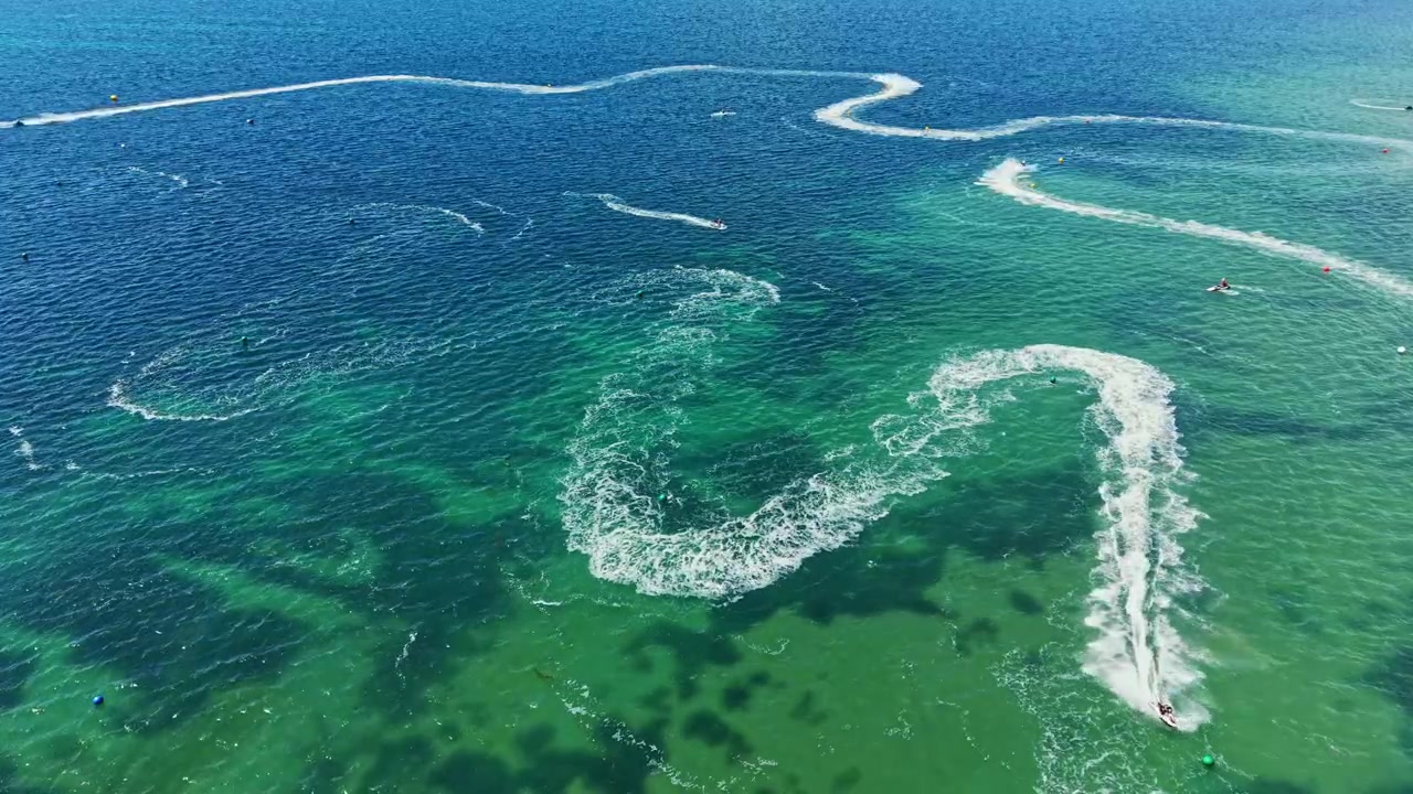 Jet ski racing takes place on a bright sunny day over clear blue water with many riders moving quickly and making sharp turns