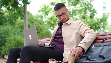 Stylish-man-using-laptop-on-bench