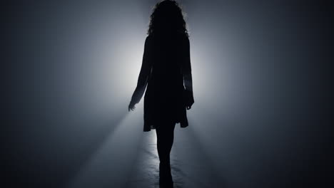 Silhouette-woman-walking-in-darkness.-Girl-walking-in-floodlight-background.