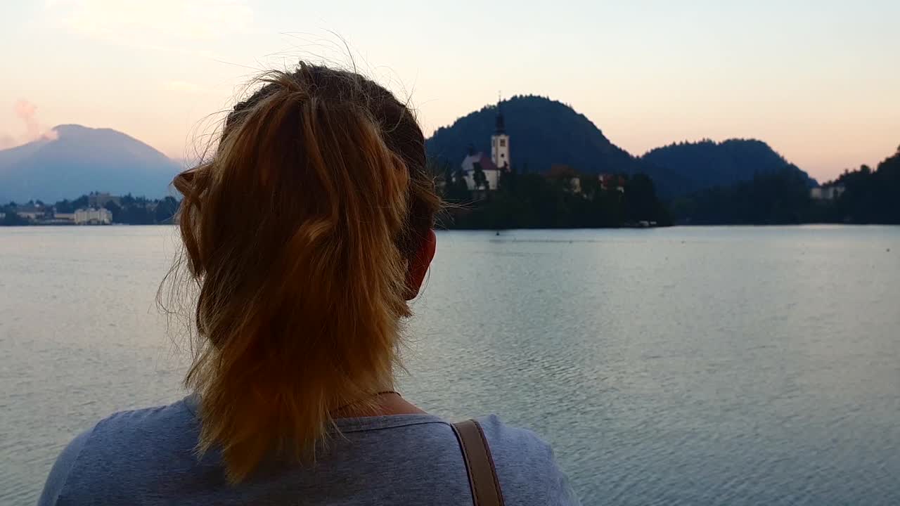 Slow motion, wide shot, of a girl, watching the church on a island, on lake bled, on a sunny summer evening, in Slovenia