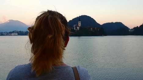 slow motion, wide shot, of a girl, watching the church on a island, on lake bled, on a sunny summer evening, in slovenia